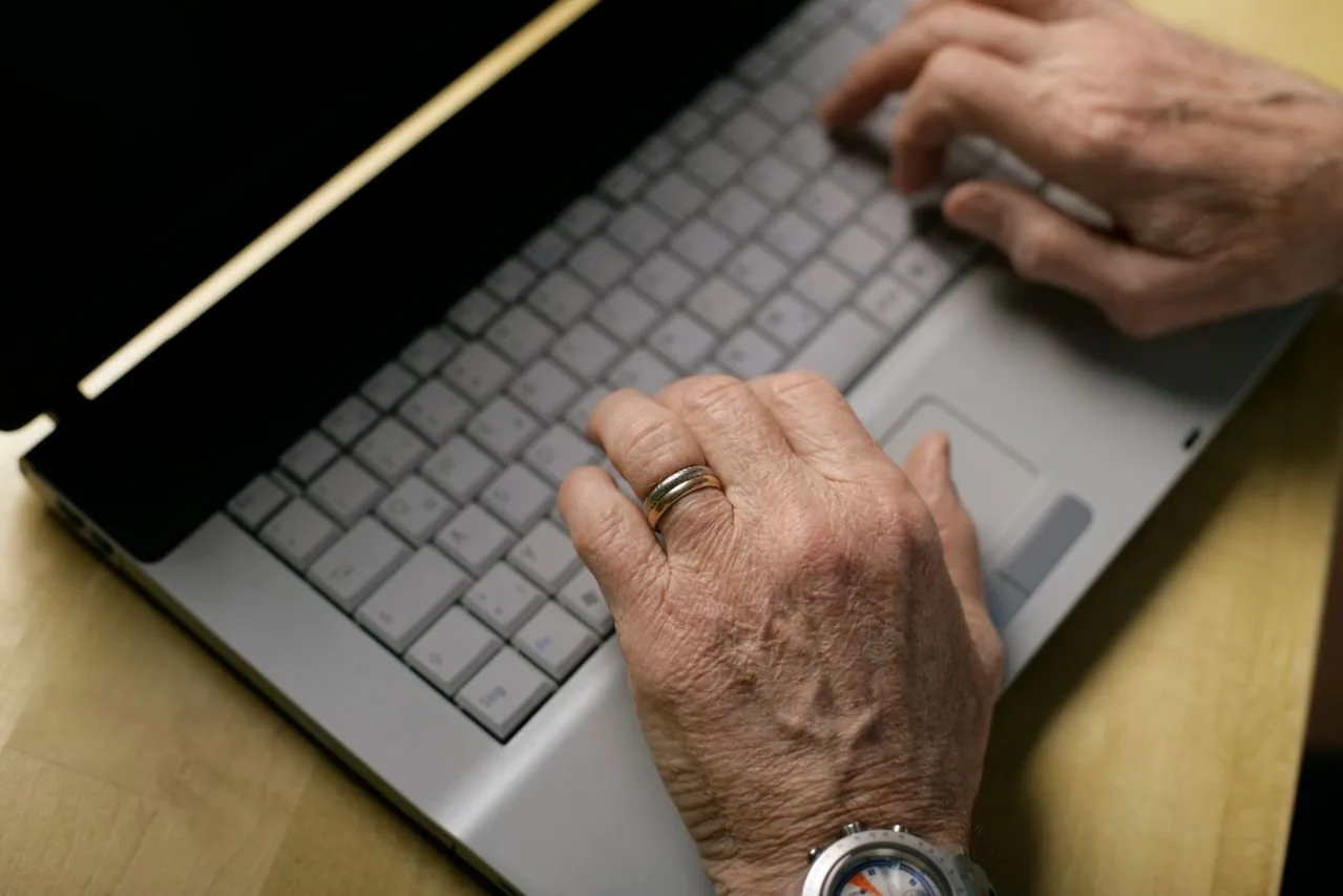 Zwei Hände einer älteren Person auf der Tastatur eines Laptops